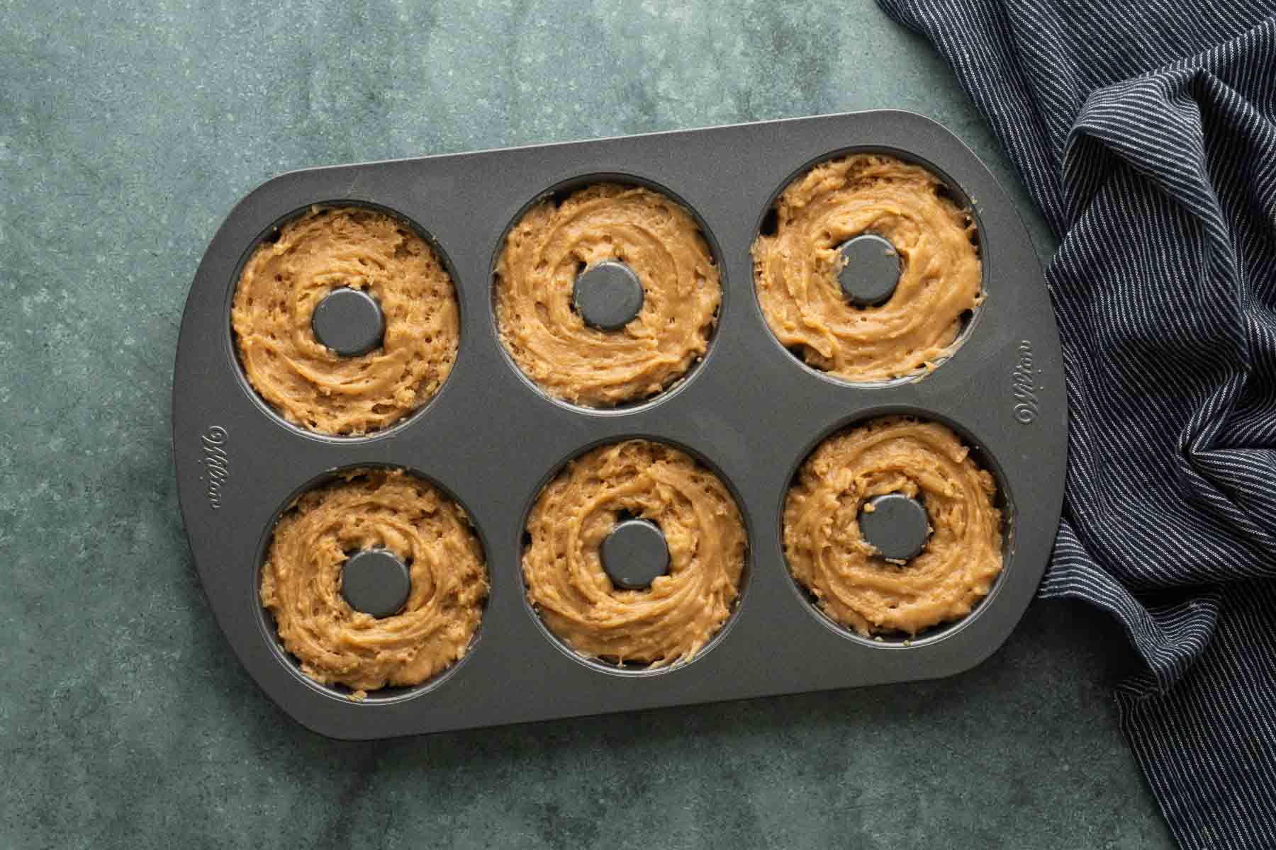 A non-stick donut pan containing six cavities filled with raw batter.